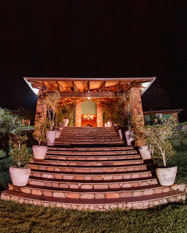 A escadaria de pedra iluminada, subindo até o pórtico de madeira, em Nova Veneza