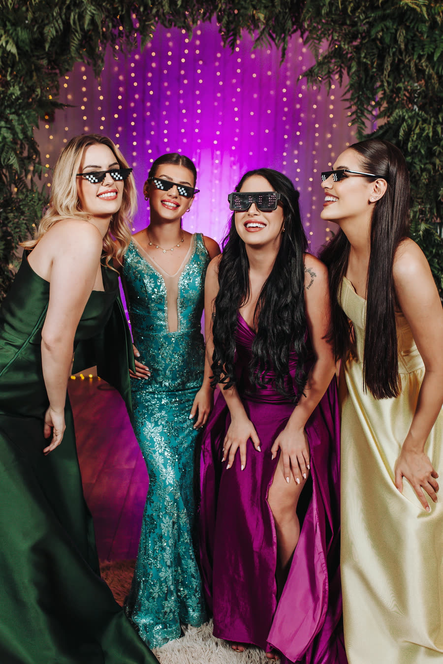 Formandas de vestido longo e óculos de festa, diante da cortina de luzes